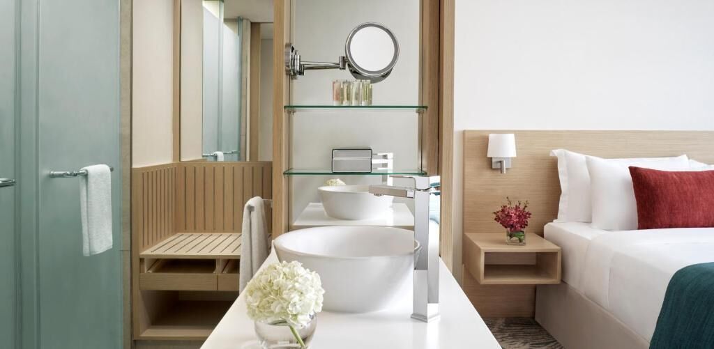 Una camera d'albergo moderna con un letto grande, un comodino con una lampada, un bagno con uno specchio ampio, un lavandino e un water.