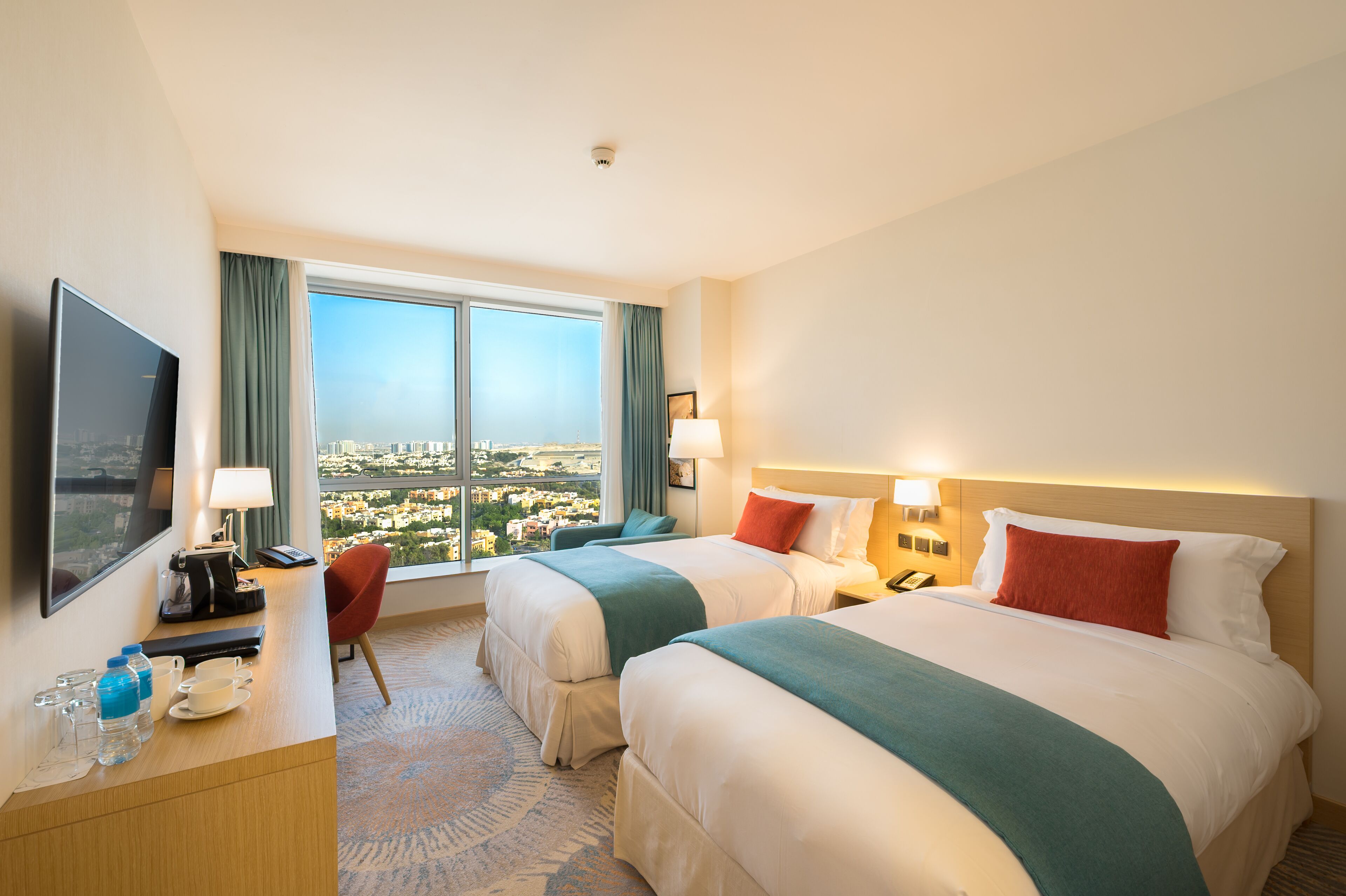 Ett hotellrum med två sängar, ett skrivbord med en tv och utsikt över stadsbilden.