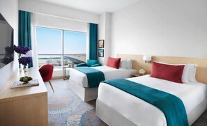 A hotel room with two beds, a desk, a chair, and a large window with a view of the airport. - Avani Ibn Battuta Dubai Hotel (Dubai)