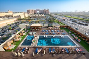 A hotel with a large swimming pool, multiple lounge areas, and a parking lot.