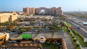 Un hotel con un amplio estacionamiento, un patio central con asientos y vistas a un paisaje urbano con un edificio de arco destacado.