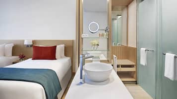 A modern hotel room with a large bed, a bathroom with a sink and mirror, and a shower area.