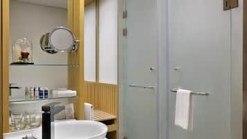 Ein modernes Badezimmer mit Duschkabine aus Glas, einem runden Spiegel und einem hölzernen Waschtisch mit Toilettenartikeln.