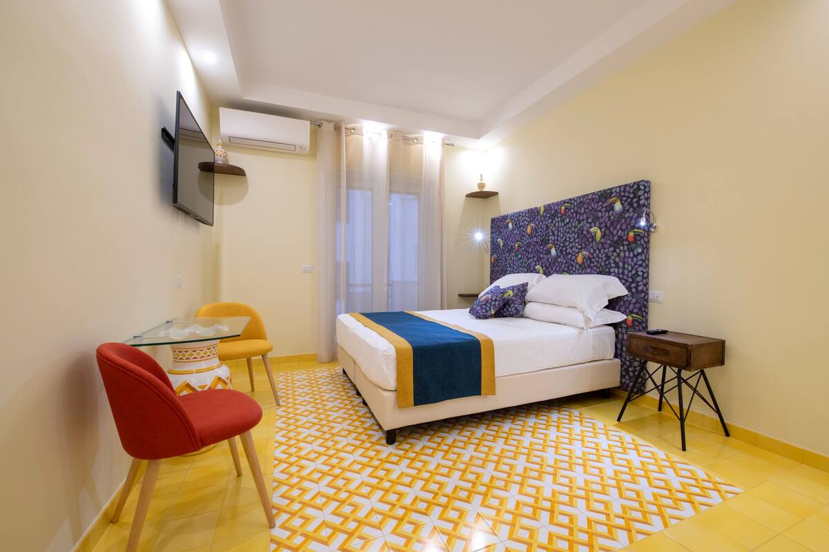 Habitación de hotel con cama, una mesita con sillas, televisión montada en la pared y piso estampado.
