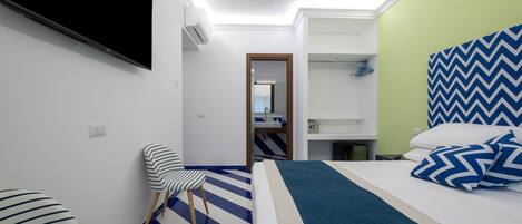 Quarto de hotel com cama, poltrona, televisão e banheiro visível por uma porta aberta.