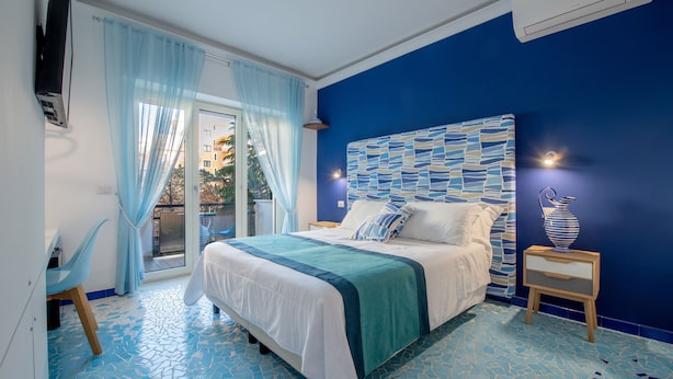 A bedroom with a bed, a nightstand, a chair, a TV, and a view of the outside. - Aquae Romanae Piazza Lauro (Sorrento)
