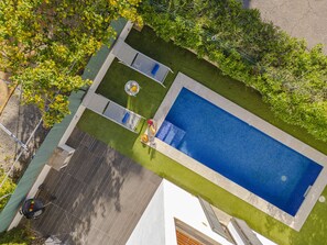 An aerial view of a backyard with a swimming pool, a patio area, and a lawn.