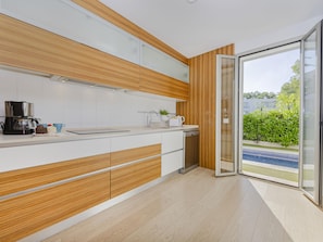 A modern kitchen with a built-in oven, a coffee maker, and a view of a swimming pool through a glass door. - Villa Salines House · Villa with private pool in Puerto de Alcúdia (Puerto de Alcudia)