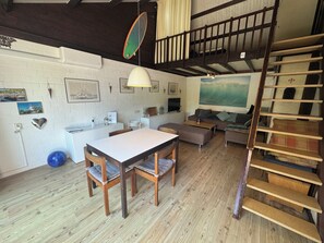 A loft-style room with a dining area, a sofa, a TV, and a staircase.