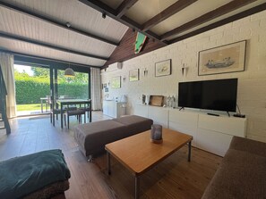 A modern living room with a sofa, a wooden table, a TV, and a dining area with a table and chairs.