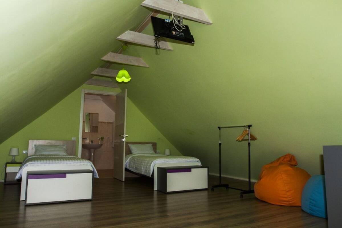 A small, triangular attic bedroom with two beds, a hanging light fixture, and a clothing rack.