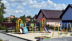 A playground with slides and swings, surrounded by a fence and houses in the background. - Perlyna Dzvinkova (Dzvinkove)