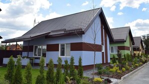 A modern two-story house with a sloped roof, a small front porch, and a well-maintained garden with young trees and shrubs. - Perlyna Dzvinkova (Dzvinkove)