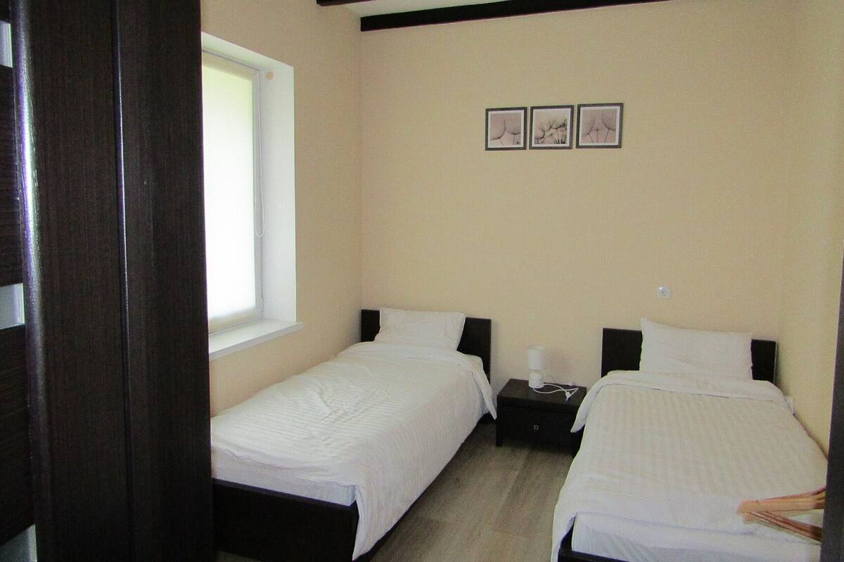 A room with two single beds, a small bedside table with a lamp, and a window.