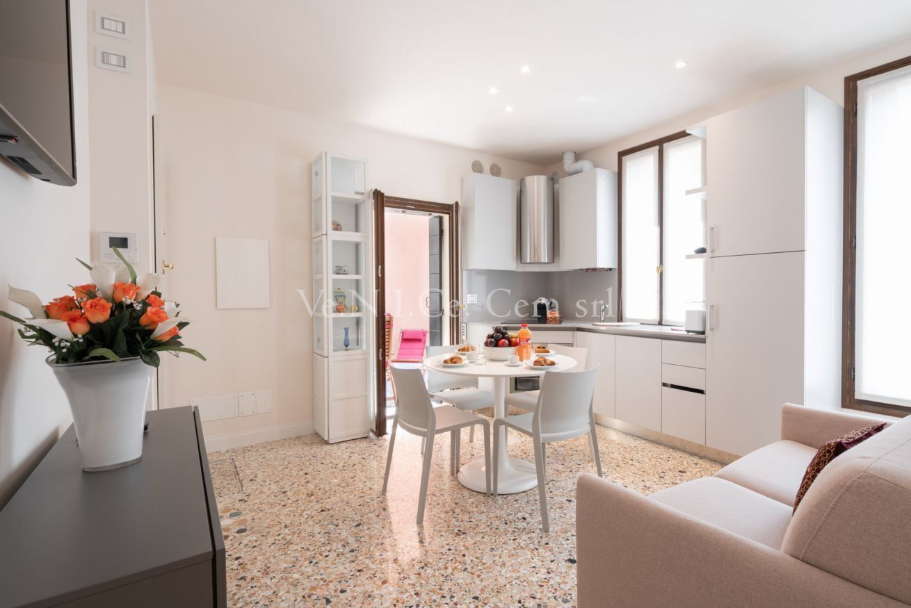 Une cuisine moderne avec des meubles blancs, une table à manger avec des chaises et une plante en pot.