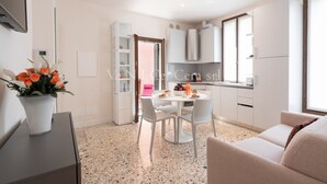 A modern kitchen with white cabinets, a dining table with chairs, and a potted plant.