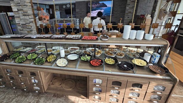 A buffet with various food items, a clock, and a television screen. - Biter Hotel (Istanbul)