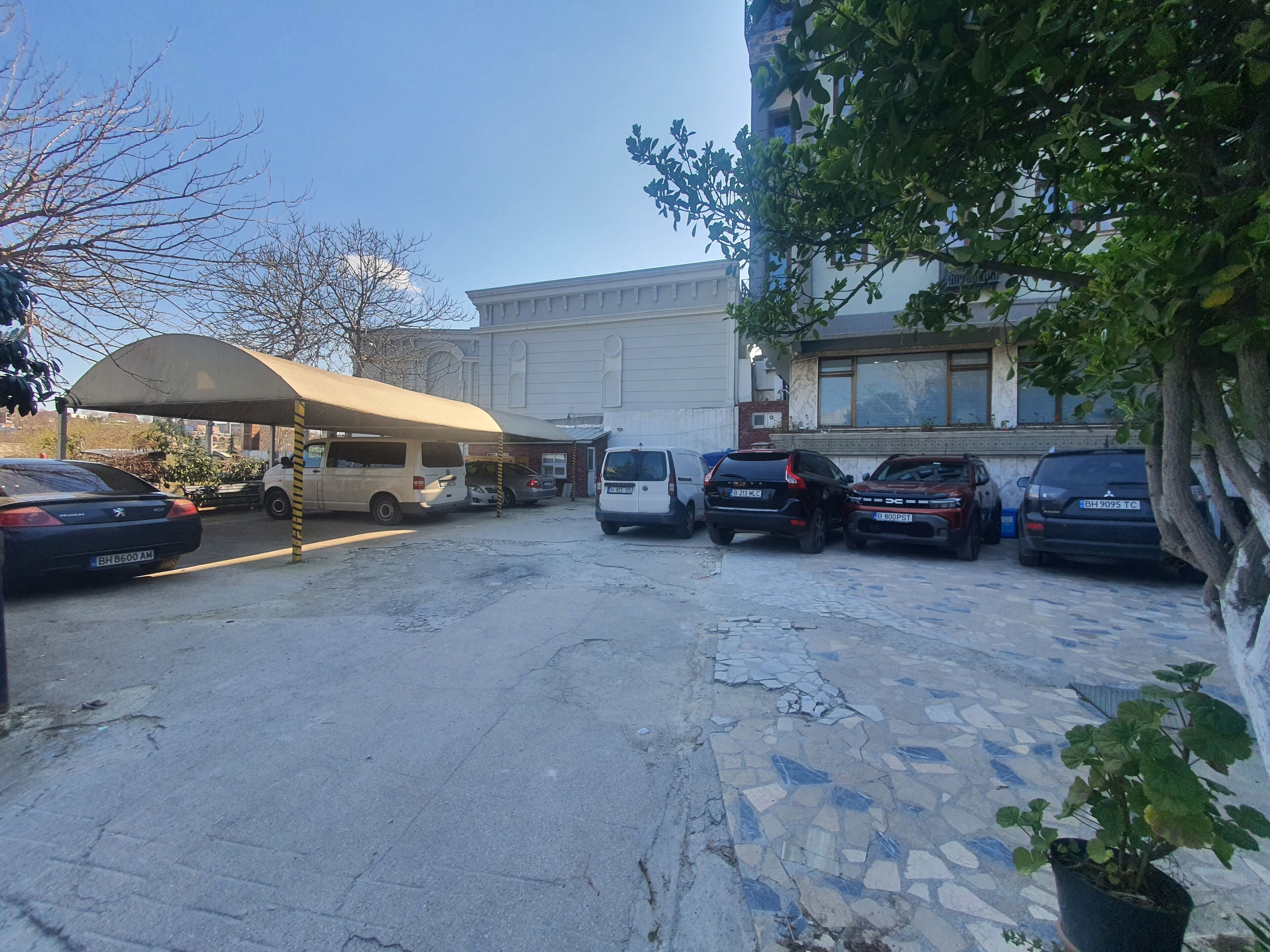 A parking area with several cars, a covered shelter, and a building with a tiled facade.