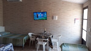 Ein Zimmer mit zwei Betten, einem an der Wand befestigten Fernseher, einem Tisch mit Stühlen und einem Fenster.