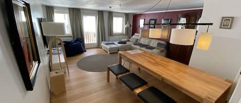 A modern living room with a wooden dining table, benches, a sofa, and a large mirror.