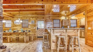 A rustic cabin-style kitchen with wooden floors, a central island with stools, and a dining area with benches.