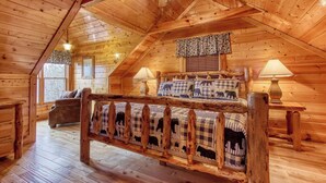 A cozy log cabin bedroom with a wooden bed, two bedside lamps, a window with curtains, and a ceiling fan.