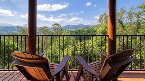 A wooden deck with two Adirondack chairs facing a scenic mountain view.