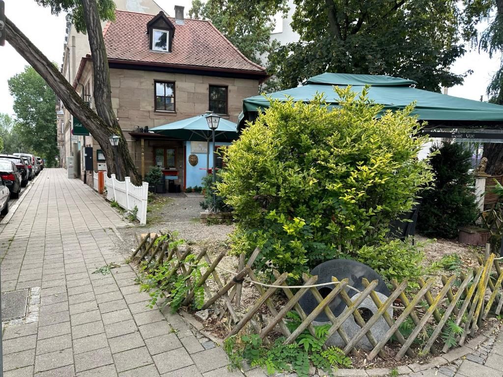 Ein Gebäude mit einem Ziegeldach, einem gepflasterten Bürgersteig und einem kleinen Garten mit Holzzaun und Busch.