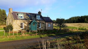A stone house with a green door, a small attached wooden structure, and a clear sky. - Bogroy  -  a cottage that sleeps 6 guests  in 3 bedrooms (Aberlour)