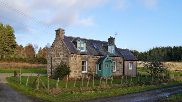 A stone house with a green door and multiple windows, surrounded by a fence and a rural landscape. - Bogroy  -  a cottage that sleeps 6 guests  in 3 bedrooms (Aberlour)