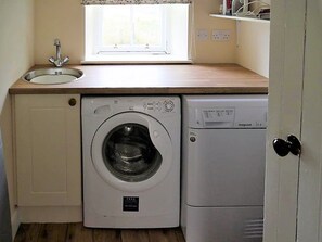 Een kleine wasruimte met een wasmachine en droger, een raam boven de wasbak, en een deur met een handgreep.