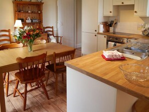 A kitchen with wooden cabinets, a dining table with chairs, a vase of flowers, and a sink with dishes.