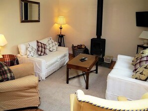 Una sala de estar acogedora con un sofá, un sillón y una mesa. También se ve una lámpara y un televisor.