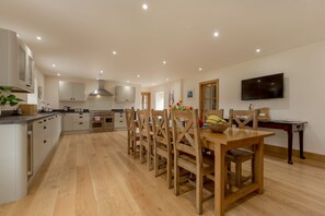 Una cocina amplia con armarios de madera, una mesa de comedor con sillas y un televisor montado en la pared.