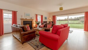 A spacious living room with a fireplace, leather sofas, and a large window offering a view of a green landscape.