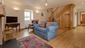 A living room with a blue sofa, wooden flooring, a television, a wooden table, and a staircase.