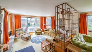 Een ruime woonkamer met een groot raam, een loungeset, een gestreept fauteuil en een houten salontafel.