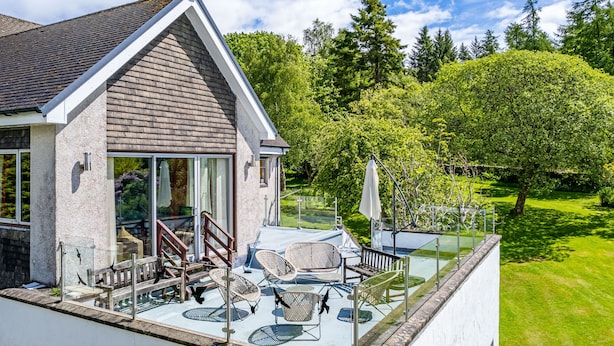 Een huis met een balkon, buitenmeubilair en uitzicht op een groen landschap.