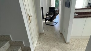 A hallway with a black lounge chair, white walls, and a door leading to a room. - Oliva: House / Villa - Oliva (Oliva)