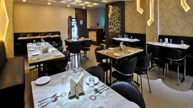 En restaurantindretning med flere spiseborde, sorte stole og et moderne loftsdesign.