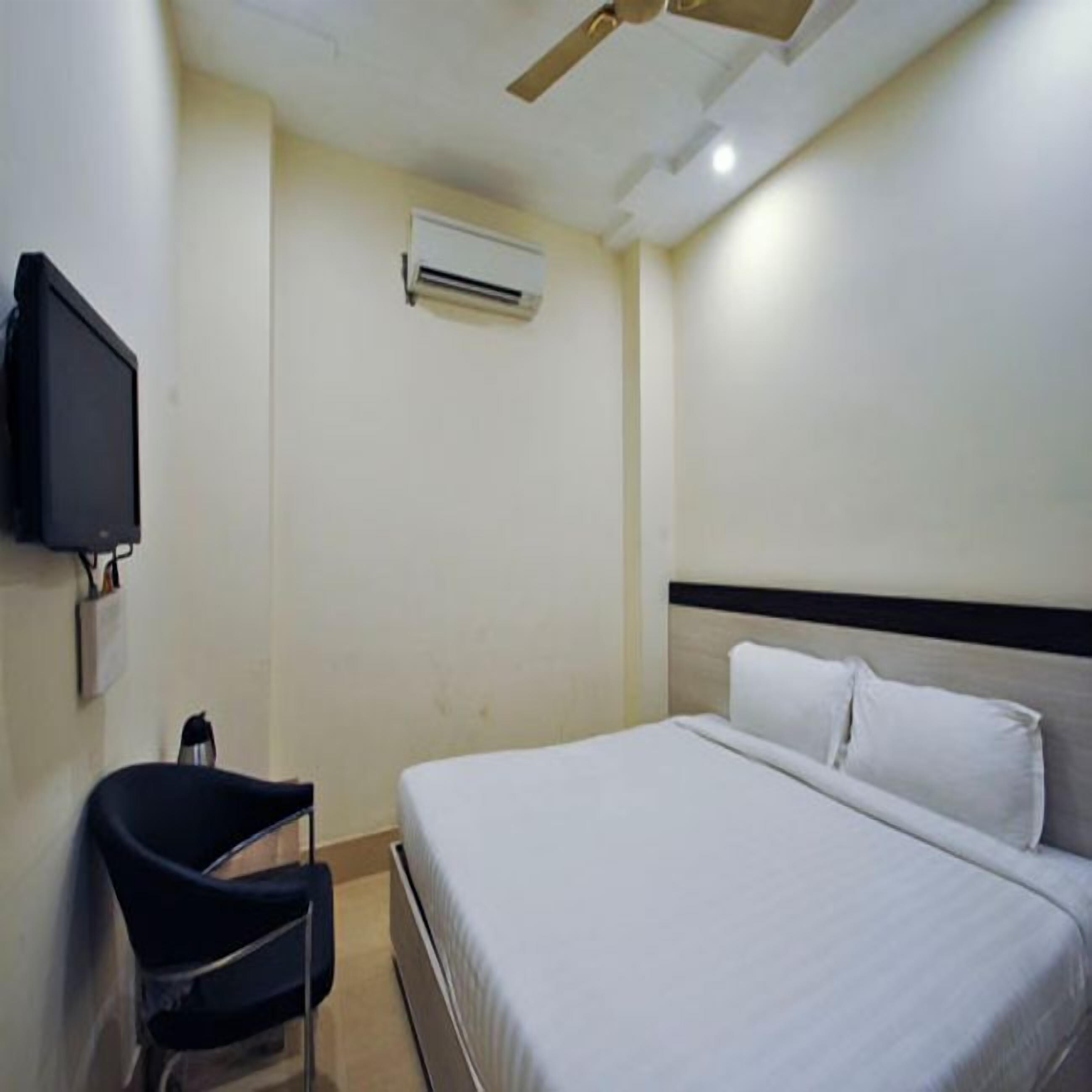 Una habitación de hotel con cama, una silla, un televisor y un equipo de aire acondicionado.