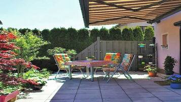 An outdoor patio with a table and chairs, surrounded by potted plants and a wooden pergola.