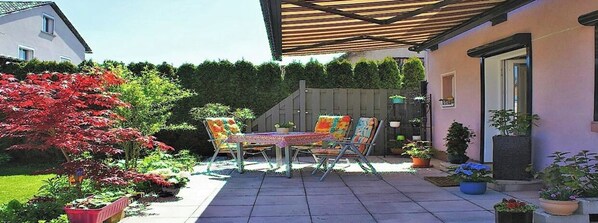 Eine Terrasse mit Tisch und Stühlen, umgeben von Blumentöpfen und einer hölzernen Pergola.