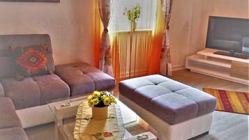 A living room with a sofa, ottoman, glass coffee table, and a TV on a stand.