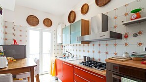 Een keuken met een gasfornuis, oven en moderne apparaten. Er is een eethoek met een tafel en stoelen.