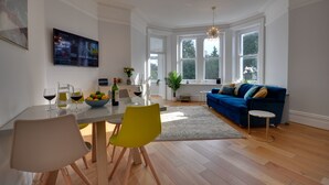 Un salon moderne avec un canapé bleu, une table à manger avec des chaises et un téléviseur fixé au mur.