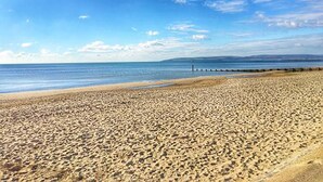 Une vaste plage de sable fin, sous un ciel bleu dégagé et une mer calme.