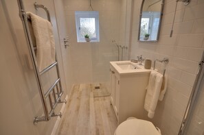 Un baño con cabina de ducha, inodoro, lavabo y una ventana con una planta.