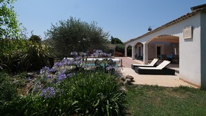 Un giardino con piscina e poltrone relax, un edificio bianco con archi e un cielo azzurro limpido.