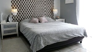 Una camera da letto con una testiera trapuntata, due comodini con lampade, un letto con coperta grigia e un quadro appeso al muro.